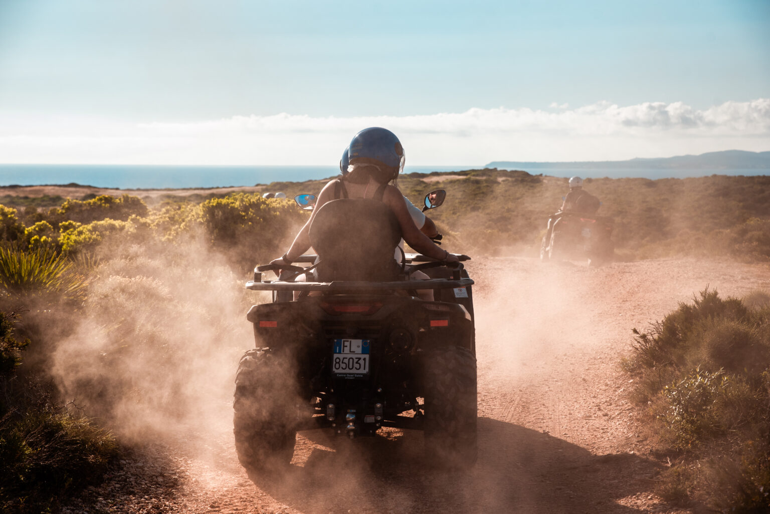 Quad con pilota e passeggero su una strada sterrata di Sant'Antioco, con il mare sullo sfondo