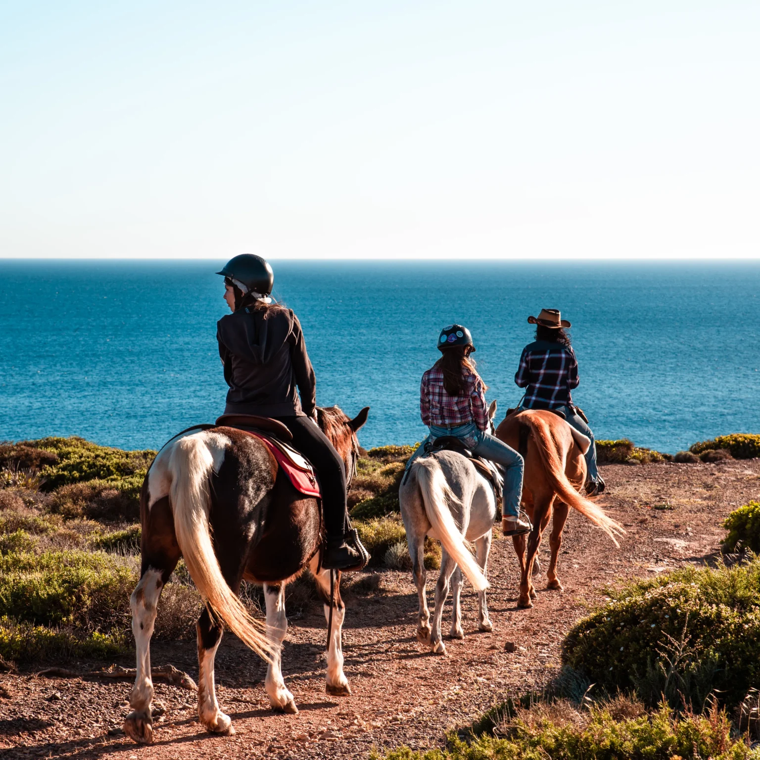 Cavalieri in fila sul sentiero costiero verso il mare, passeggiata a cavallo Arco dei Baci
