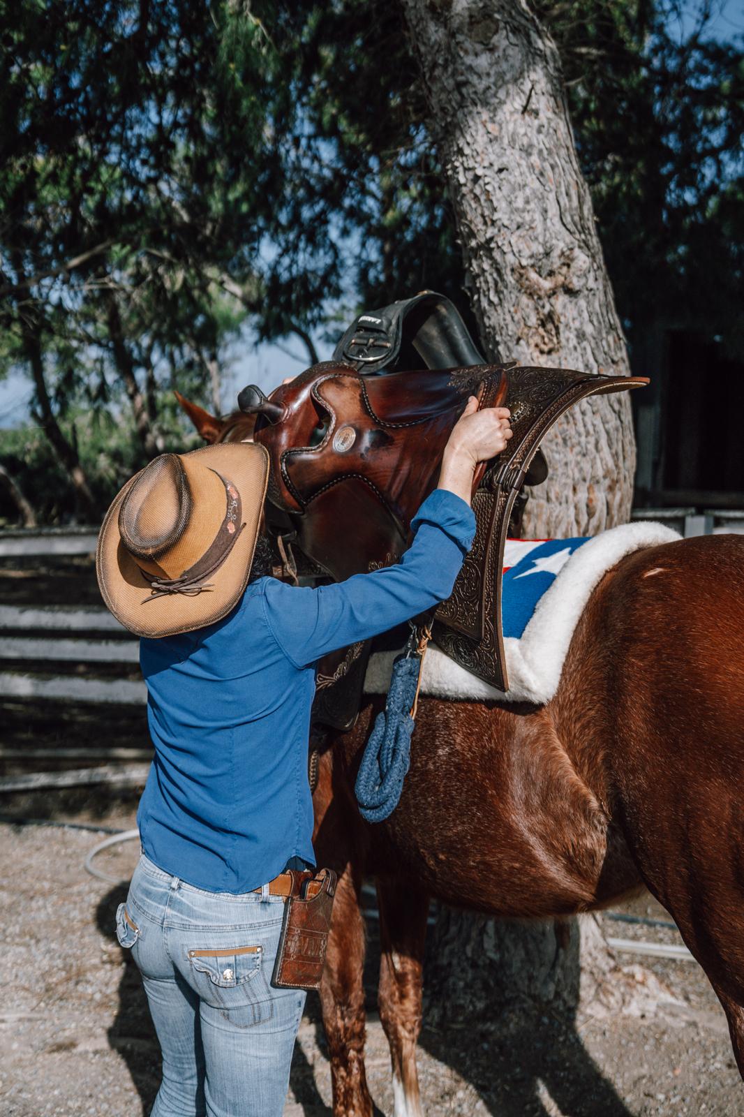 Un'ospite con il cappello da cowboy sistema la sella western sul cavallo al ranch